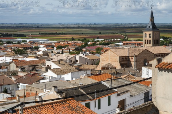 A town view with red roofs and a church tower in the distance under a cloudy sky, Campo de