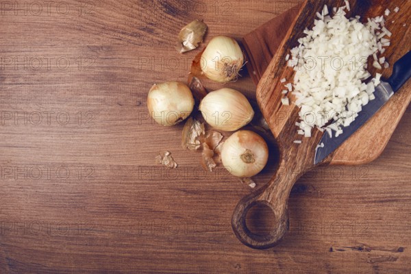Finely chopped onion on a chopping board with a knife, wooden table, top view, no people