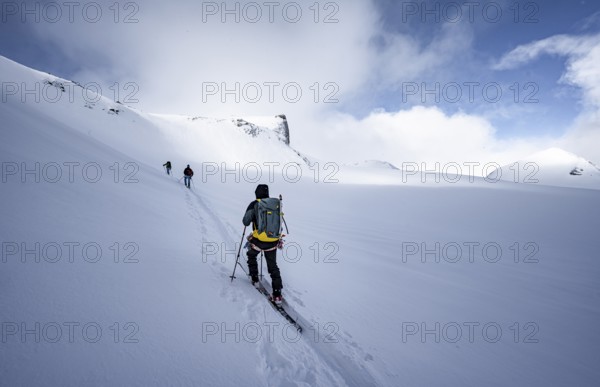 Three ski tourers in a snowy mountain landscape, ascent to the Wildhorn, cloudy mood, high tour,
