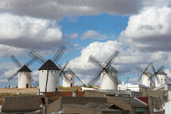 Several mills in a rural area, with old buildings in the foreground and a cloudy sky above, Campo