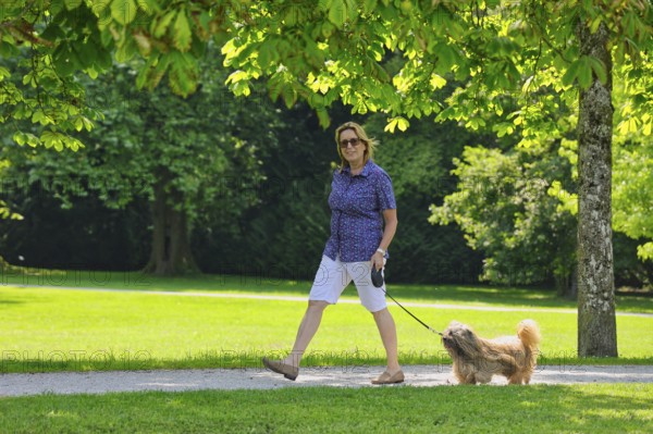 Woman takes Lhasa Apso for a walk in the park