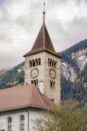 A traditional stone church tower in front of an autumnal wooded mountain, Lake Brienz, Switzerland,