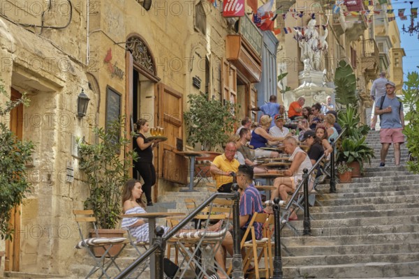 Tourists enjoy a break on the steps of the St. Lucia Street, Valletta, Malta, Europe