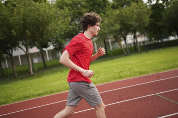 Side view of a young caucasian man running with tired expression along a running track