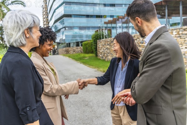 Multi-ethnic businesswomen shaking hands during outdoor meeting next to business colleagues in the