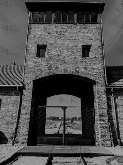 A historic brick building with a watchtower and gate, featuring rail tracks in front.