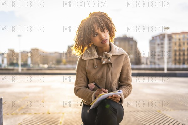 Pensive beauty latin woman writing notes sitting on the city with urban landscape on the background
