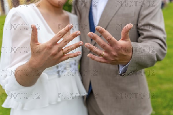 A couple is posing for a picture with their wedding rings. The man is wearing a suit and tie, while