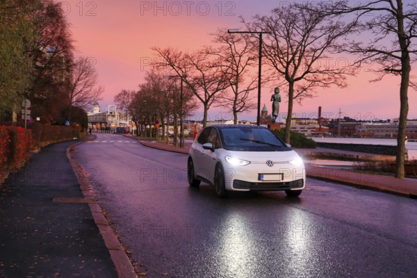 White Volkswagen ID3 electric car driving on seaside street at beautiful morning dusk, copy space.