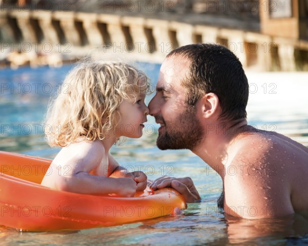 Happy child playing with father in blue water of swimming pool on a tropical resort at the sea.