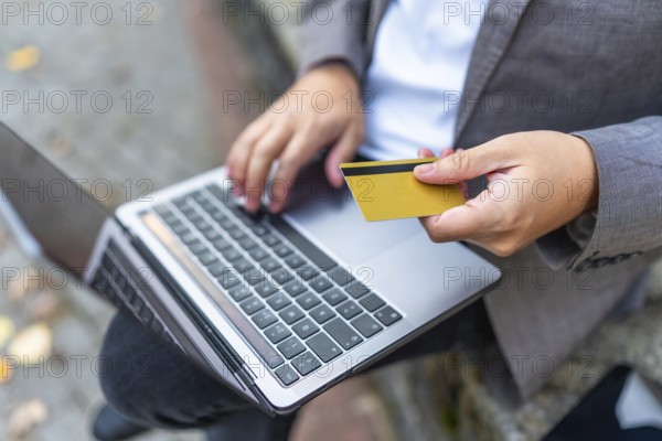 Close-up of a caucasian man shopping online using laptop and credit card sitting on city bench