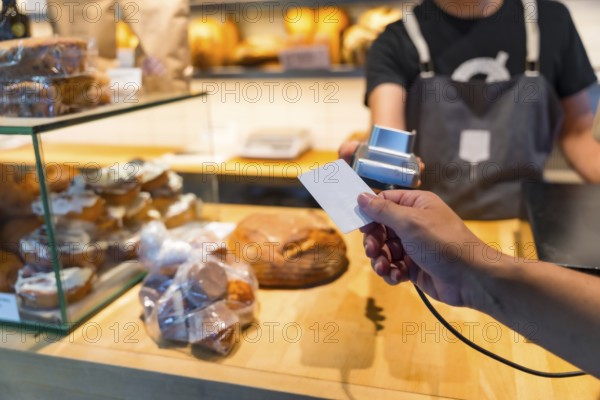Customer in the bakery shop buying an artisan bread from the baker in the workshop, paying with the