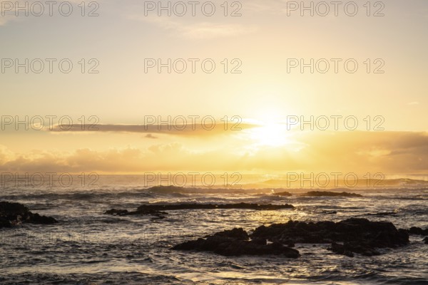 Sunrise over the sea with gentle waves. Sandy beach with lava rocks and blue water alternating with