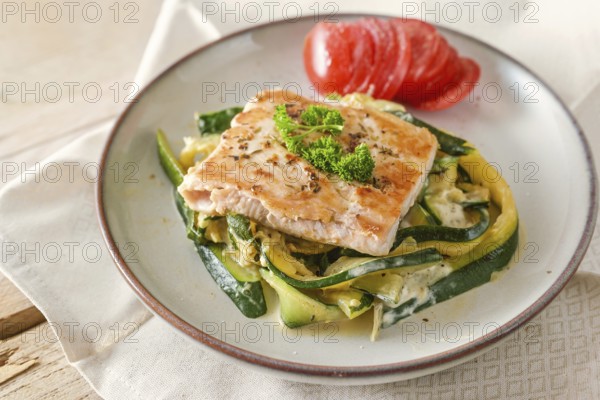 Fried wild salmon with parsley garnish on zucchini vegetables and fresh tomato on a light plate,