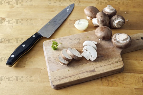 Mushrooms whole and sliced on a wooden cutting board and a kitchen knife, preparation for cooking a