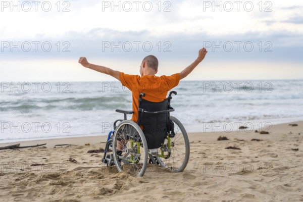 Disabled person on his back in a wheelchair on the beach with open arms enjoying the freedom