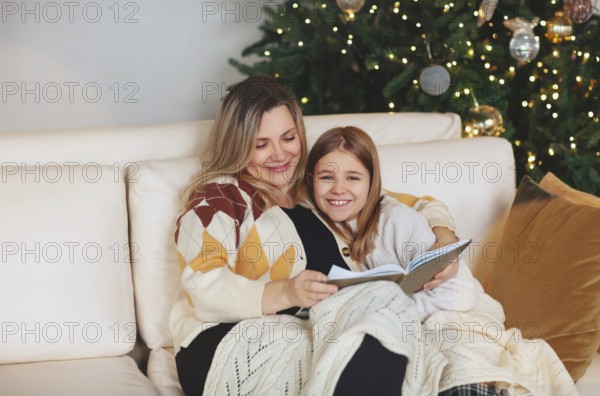 Happy family grandmother and little girl daughter sitting together on sofa and reading book while
