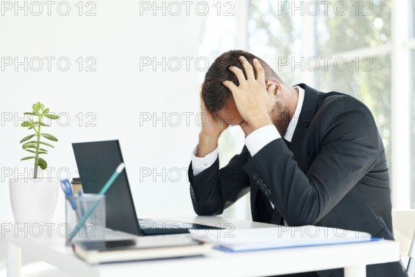 Stressed tired businessman sitting at the desk in creative office. Man suffer from headache,