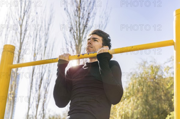 Attractive man doing pull-ups exercises on a crossbar in a public park