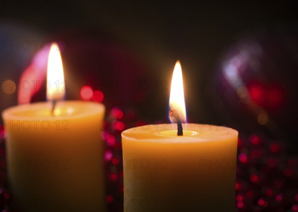 2 lit candles in front of Christmas decorations