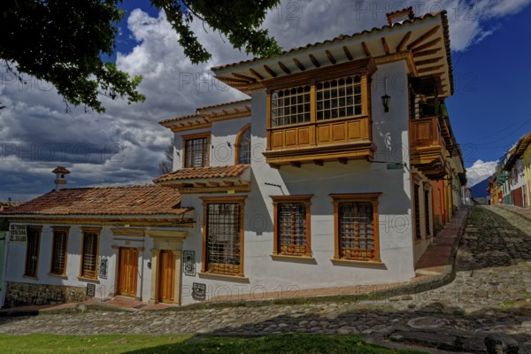 Traditional white house with wooden windows on a cobblestone street under a cloudy sky, Historic