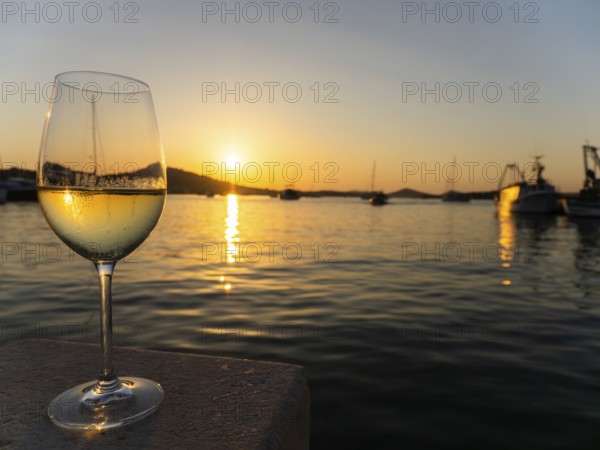 Sunset shimmering through a glass of white wine, evening mood in the harbour, boats and sailing