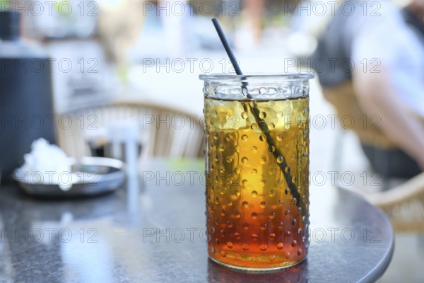Refreshing iced tea with lemon syrup and a drinking straw in a glass in a street cafe in the