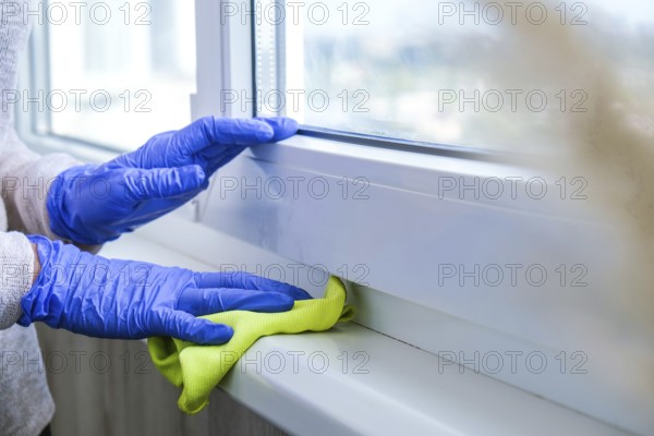 Cleaning the windowsill wiping dust by blue microfiber cloth for cleaning on the glass window rail