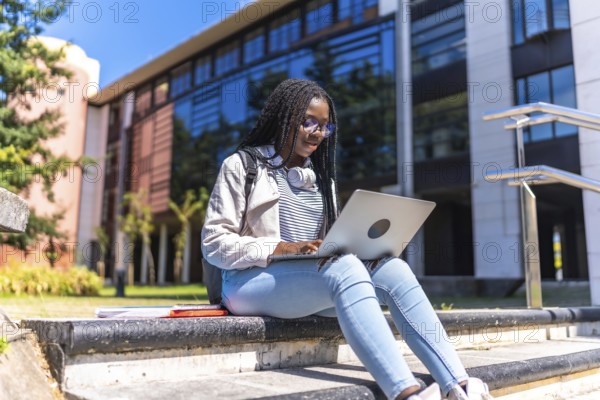 Focused female african university student using laptop sitting on outdoors staircases in the campus