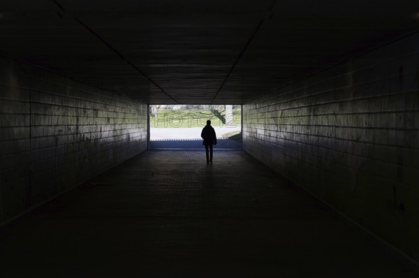 silhouette of a person walking through a dark underpass symbolizing light at the end of the tunnel