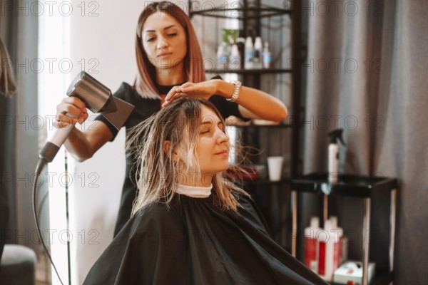 Happy woman with stylist making hairdo at salon. Competent female hairdresser deciding what to do