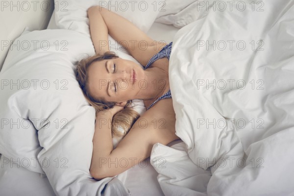 Woman sleeping in bed under white quilt with head on pillow