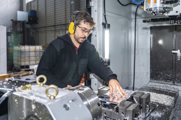 Manual worker with protective goggles and headphones using a milling cnc modern machine