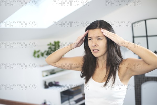Attractive young woman with a migraine headache standing holding her fingers to her temples with