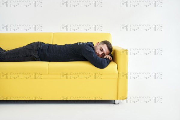 Tired young man lying down on yellow sofa over white background. Exhausted concept