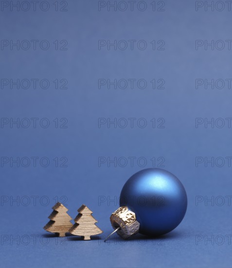 Blue Christmas tree ball with small wooden tree shapes on a blue paper background with space for