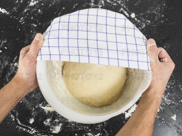 Person covering a dough for proving in a bowl on black table