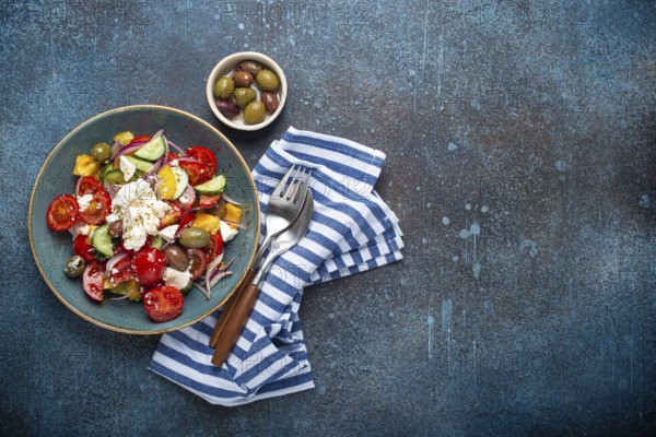 Greek fresh healthy colorful salad with feta cheese, vegetables, olives in blue ceramic bowl on