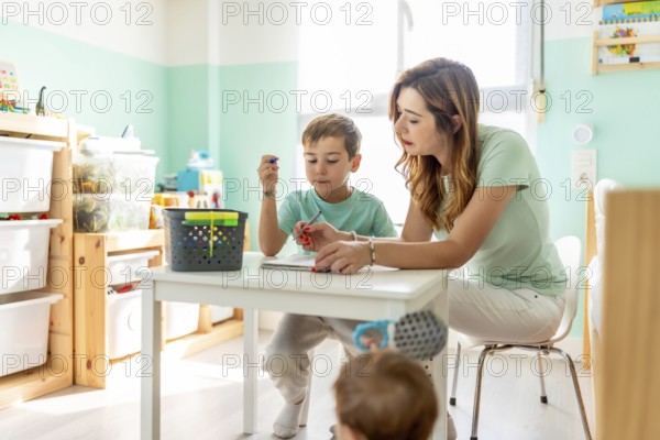 Mother and school boy draw color pencil in the bedroom next to a baby boy