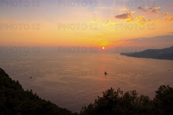 Looking down from Alanya Castle, the orange-red evening sun falls into the sea on the horizon of