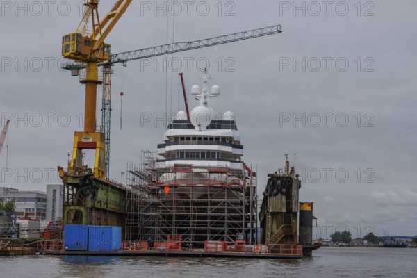 A large ship being repaired or rebuilt in a shipyard, surrounded by scaffolding and cranes,