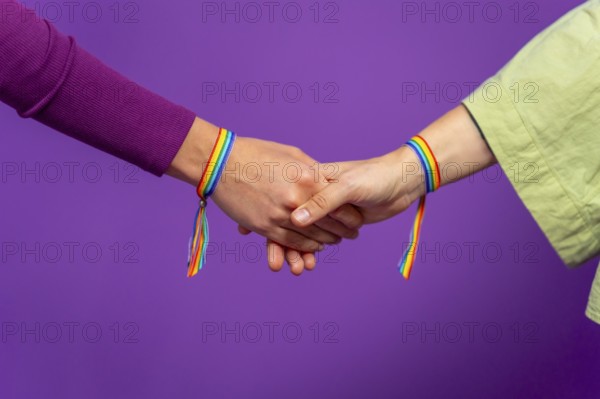 Studio photo with purple background and close-up of two lesbian woman holding hands wearing lgbt