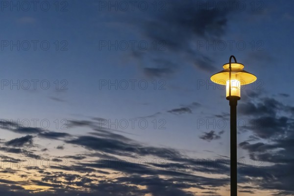 Illuminated street lamp in front of a rainy autumn sky