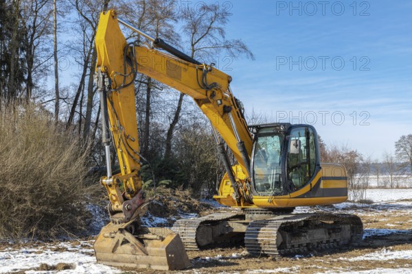 Large excavator parked in a meadow in winter