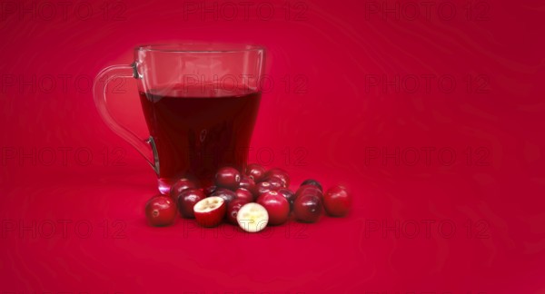 Red cranberries and transparent cup containing a dark red cranberry juice against a vibrant red