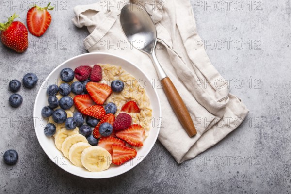 Oatmeal porridge with fruit and berries in bowl with spoon on white wooden background table top
