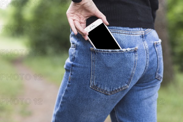 Woman removing smartphone from blue jeans pocket