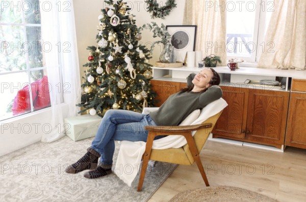 Happy woman with mug of tea in hands looking out of kitchen window at winter landscape outside.