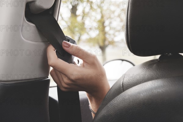 A woman's hand reaches behind her seat belt to fasten it. The concept of safe driving of women by
