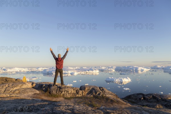 Ilulissat, Greenland, July 7, 2018: Young man looking at the Ilulissat Icefjord during midnight sun